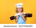 Small photo of Kid chef cook with cooking pot stockpot. Child cooking, little chef prepares food. Kid boy in chefs hat and apron on yellow studio isolated background.