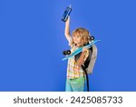 Child boy holding longboard and water bottle on blue isolated background. Kid with pennyboard. Studio shot of cheerful little fashion kid with penny board.