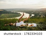 Gorgeous young girl in a white sundress lying on grass and having a picnic in a picturesque place. Romantic picnic. Happy beautiful girl on the nature picnic. Relaxing girl in nature.