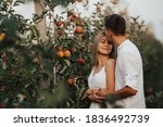 Happy bride and groom with closed eyes standing in embrace near trees in apple orchard. Man tenderly kissing him bride on the 
forehead.