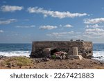 Bunker on the east coast of Atlantic ocean (Africa side). Still vivid memory, many artificial flowers. Atlantic ocean and blue sky with white clouds. Fuerteventura, Canary Islands, Spain.