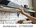 Cropped view of woman hand select mode on cooking hood, standing near kitchen appliance in contemporary interior with brick wall and decor on shelves at blurred background