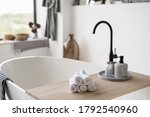 Selective focus on clean folded towels at wooden shelf on empty and contemporary tub with modern black water tap on blurred background. House decor at bright home with white interior design