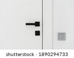 Close up view of light switch on the white wall near modern minimalist door with black handle. Contemporary interior design details at home, apartment or office