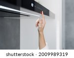 Cropped shot of woman using cooker hood in minimalist modern kitchen with modern integrated appliances, female pressing button on cooking extractor while preparing food at home