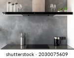 Reflective countertop with built-in induction cooker, exhaust hood with touch controls and glasses on top of it, set of knives and black kettle in modern kitchen in contemporary appartment