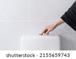 Small photo of Cropped view of woman's hand pushing button and flushing toilet in bathroom. Everyday routine. Flush cleaning toilet. Contemporary facilities for people