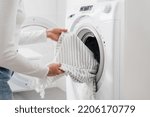 cropped shot of female hands put bed linen or cotton towel in automatic washing machine with open door in bathroom, housekeeping duties