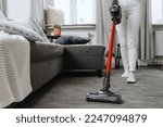 cropped shot of housewife in white jeans using cordless handheld vacuum cleaner in living room with sofa and pillows, household chores concept