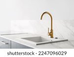 detail in interior at luxury kitchen with golden shiny faucet and rectangular sink built in marble countertop on wall background with copy space