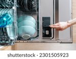 Top view of opened dishwasher machine with plastic detergent compartment and chemical tablet. Washing tableware. Full loaded rack. Modern appliance in kitchen