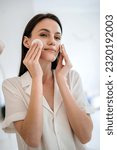 Small photo of Female cleansing her face with cosmetic lotion using cotton sponge. Lady remove makeup at evening by mirror in bathroom. Caring for skin. Young woman do everyday facial skincare procedure at home