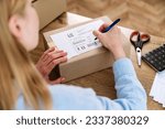 Woman hand writing address for delivery, filling information on parcel box. International shipping products to customers. Carton package with label. Fast logistic service.