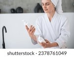 Small photo of Cropped view of woman in robe holding and choosing skincare products. Bottles with pumps. Organic, natural cosmetics for daily routine. Beauty and wellness concept.