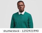 Small photo of Angry dissatisfied black man frowns face has disappointed facial expression, vexed look, dressed in green jumper, discontnent with changing job position, isolated over white studio background