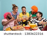 Small photo of Football fans, happiness and fun concept. Overjoyed friend glad have success on football bet, win lump sum of money, hold dollars, eat tasty snack, sit around table, laugh loudly, isolated on blue
