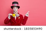 Small photo of Smiling glad hatter in fashionable costume has aristocratic manners drinks tea and indicates at copy space isolated over rosy background. Man has image of classic tale character for halloween