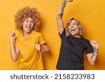 Small photo of Studio shot of happy lively young women enjoy life shake arms feel energetic exclaim loudly wear casual basic t shirts isolated over yellow background have fun and dance. Happy emotions concept