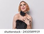 Small photo of Gender fluid man with vivid makeup and manicure wears black corset and chain around neck smiles broadly being positive comes on party for gays isolated on white background. Non traditional orientation