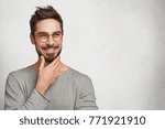 Small photo of Good looking male with appealing smile has thoughtful cheerful expression, keeps hand under chin, plans how to spend lump sum of money which he earned, isolated over white background, copy space