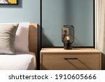 Closeup of modern black metal edison bulb lamp on wooden bedroom night table in contemporary style gray room interior with pine wood bed and white cotton bedlinen