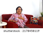Small photo of Senior elderly asian woman with breathless while sitting on the sofa at home with copyspace