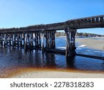 An old train bridge stretching across water at low tide on a winter day.
