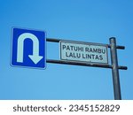 a traffic sign symbolizing a U-turn with an Indonesian-language warning that reads obey traffic rules. Photo of a traffic sign with a blue sky background