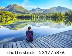 Beautiful young girl sitting near by clear lake under wonderful mountains in High Tatras - Slovakia. Morning light on Strbske pleso lake. Photo before touristic trip. Freedom concept 