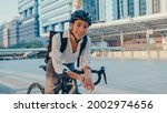 Asian businesswoman go to work at office stand and smiling wear backpack look at camera with bicycle on street around building on a city. Bike commuting, Commute on bike, Business commuter concept.