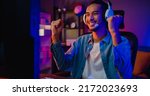 Small photo of Happy asia guy gamer wear headphone participation play video game colorful neon lights computer in living room at night modern house. Esport streaming game online, Home quarantine activity concept.