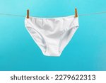 white washed women's panties made of cotton with clothespins hanging on a rope on a blue background