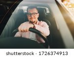 A young europen beautiful smiling man wearing glasses driving a car in the sity on sunset. View through the windshield 