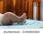 Small photo of close-up detail of the feet of a latina baby girl lying on a bed with blue sheets. feet of a chubby baby girl, with kicking motion and shrunken toes.