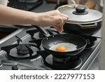 Small photo of detailed shot of a woman's hand adding salt to the egg she is frying in a frying pan on the burner of a gas stove in a Colombian kitchen.