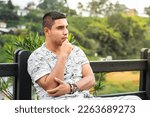 young Latino man, thinking and looking for new ideas, sitting on a chair in an outdoor park.
