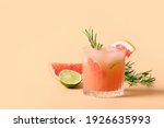 Small photo of Grapefruit soda with lime garnish rosemary sprig on color beige background. Mocktail Paloma. Close up.