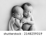 Small photo of Tiny newborn twins boys in white cocoons on a white background. A newborn twin sleeps next to his brother. Newborn two twins boys hugging each other.Professional black and white studio photography.