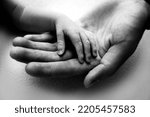 Small photo of A parent holds the hand of a newborn child. The small hand of the son with tiny fingers lies on the palm of the father. The concept of a happy family. Family hereditary ties. Black and white photo.