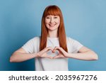 Cute girl making heart with fingers chest smiling on blue background