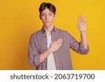 Small photo of Photo of young guy hand on chest make oath promise tell the truth isolated over yellow color background