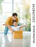 Small photo of Happy asian family, father having fun with son while pushing carton box in living room.Young family enjoy moving to new home on relocation day.