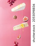 Small photo of Flying cheese. Brie cheese with honey on a pink background.