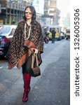 Small photo of LONDON - FEBRUARY 15, 2019: Nurce Erben wears sunglasses, a Fendi logo poncho, a necklace, a Fendi bag, red high leather boots, during London Fashion Week February