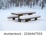 A deep, heavy layer of untouched, fresh, fluffy white snow covers the picnic tables and benches in the nature park.
