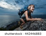 Hiker with backpack climbing natural rocky wall on a dark cloudy background. There are water drops on the skin