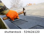 Worker hands installing bitumen roof shingles using hammer in nails.