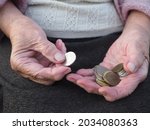 Small photo of Old wrinkled hands hold a coin. Pensioners count pennies, living wage, poverty and survival. Basic income below the poverty line. Economic problems of old people, lack of money.
