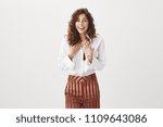 Woman surprised being chosen best worker of month, smiling broadly and blushing from happiness and amazement, pointing at herself, laughing, feeling joy while standing over gray background