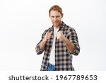Small photo of Daring and confident smiling redhead man ready for fight, holding fists raised beckon you to box, fighting with someone. Sportsman in casual clothes defending himself, white background